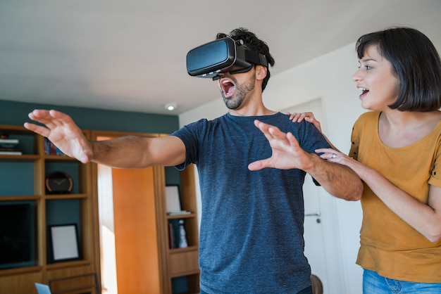 Retrato de pareja joven divirtiéndose juntos y jugando videojuegos con gafas VR mientras se queda en casa