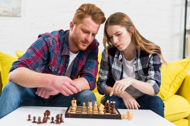 Retrato de una pareja joven jugando al ajedrez de madera juntos en casa