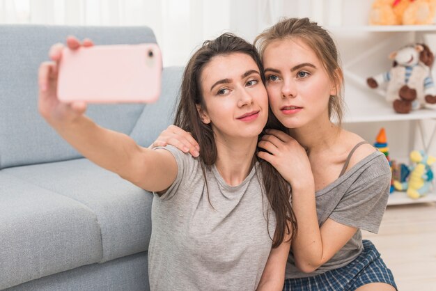 Retrato de pareja joven lesbiana tomando selfie en smartphone en casa