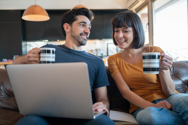 Retrato de pareja joven pasar tiempo juntos y usando la computadora portátil mientras está sentado en el sofá en casa