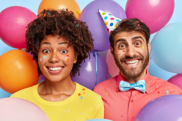 Retrato de pareja joven posando rodeada de globos de colores de cumpleaños