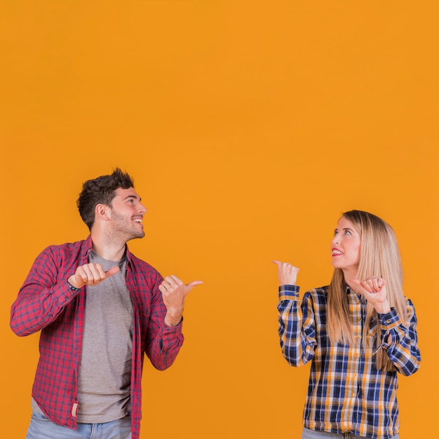 Foto gratuita retrato de una pareja joven que muestra el pulgar hasta la espalda contra un fondo naranja