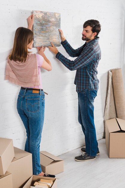 Retrato de una pareja joven sosteniendo un marco pintado sobre la pared blanca en su nueva casa