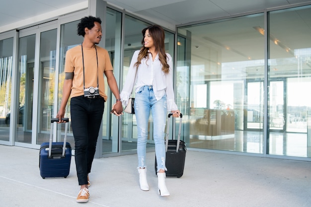 Retrato de pareja de jóvenes turistas llevando maleta mientras camina al aire libre en la calle. Concepto de turismo.