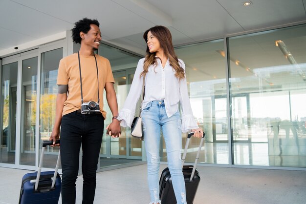 Retrato de pareja de jóvenes turistas llevando maleta mientras camina al aire libre en la calle. Concepto de turismo.