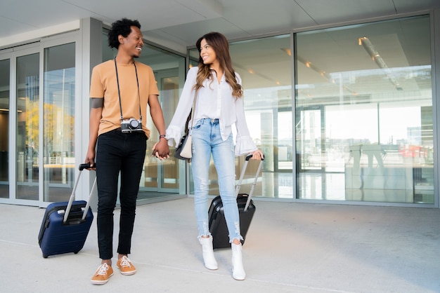 Retrato de pareja de jóvenes turistas llevando maleta mientras camina al aire libre en la calle. Concepto de turismo.