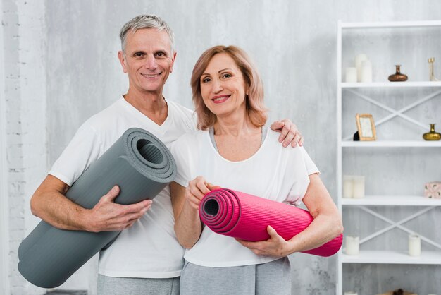 Retrato de una pareja mayor sana con estera de yoga de pie en casa