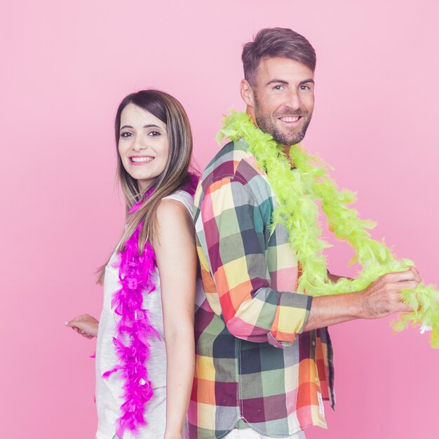 Retrato de pareja de pie espalda con espalda con boa alrededor de su cuello contra el fondo rosa