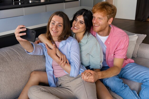 Retrato de pareja poliamorosa en casa tomando selfie en el sofá