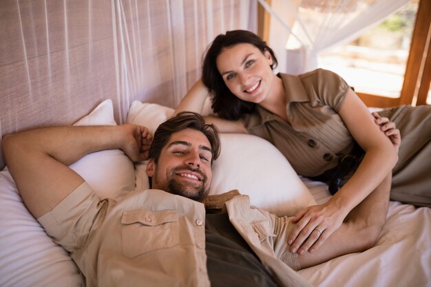 Retrato de pareja sonriendo mientras está acostado en la cama con dosel