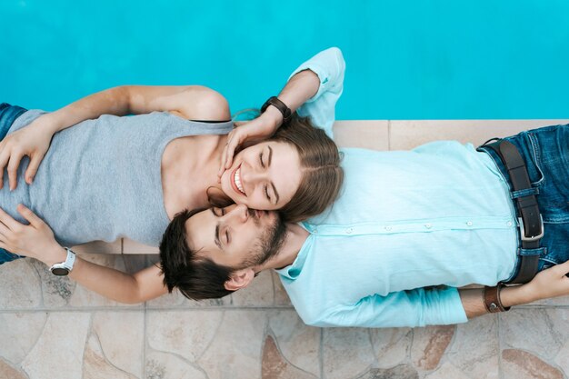 Retrato de pareja sonriente acostado vestido cerca de la piscina. Se adoran