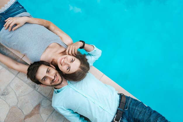 Retrato de pareja sonriente acostado vestido cerca de la piscina. Se adoran