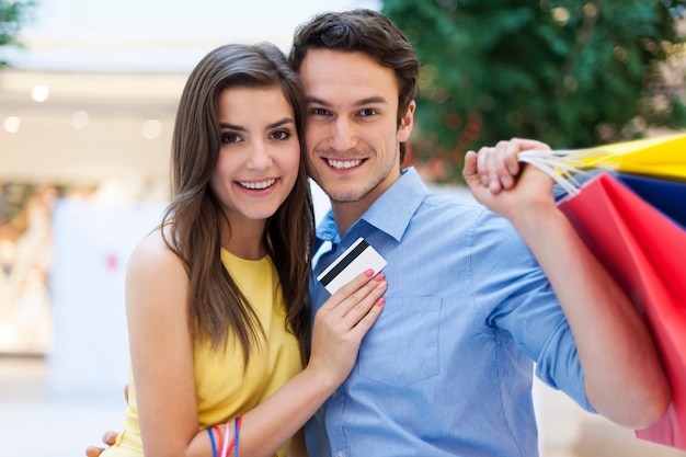 Retrato de pareja sonriente con tarjeta de crédito y bolsas de la compra.