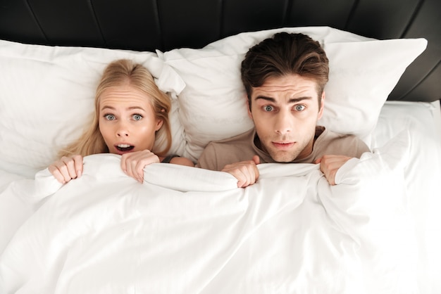 Retrato de pareja sorprendida acostada en la cama y cubrir con una manta