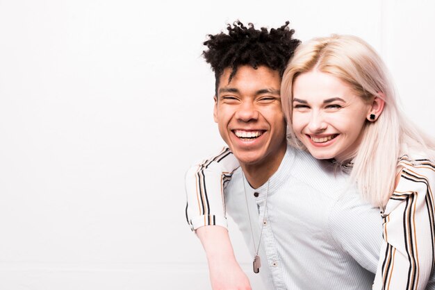 Retrato de los pares adolescentes interraciales sonrientes que miran la cámara contra el contexto blanco