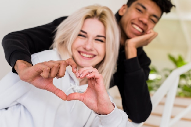 El retrato de los pares interraciales jovenes sonrientes que hacen el corazón forma con sus manos