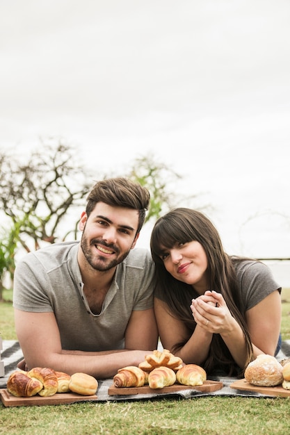 Retrato de los pares jovenes sonrientes que mienten en la manta con pan cocido en la bandeja de madera