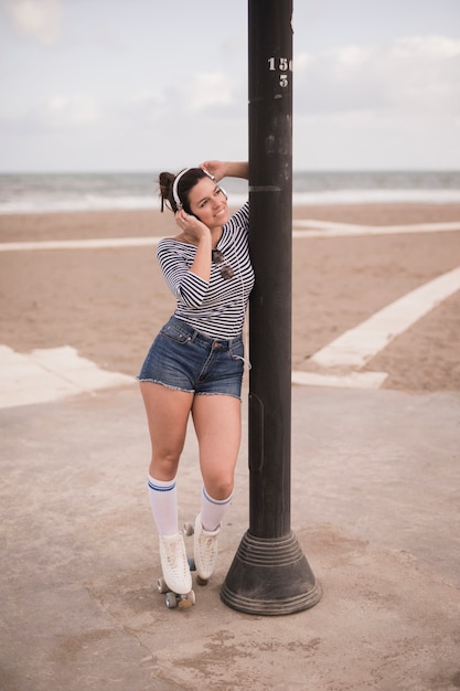 Foto gratuita retrato de un patinador femenino sonriente que se coloca cerca del pilar del hierro