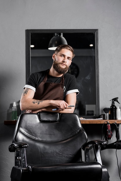 Foto gratuita retrato de un peluquero masculino de pie detrás de un sillón negro