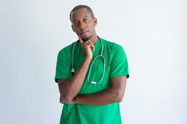 Retrato de pensativo joven médico general con la mano en el mentón.