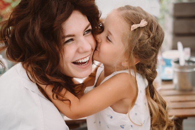 Retrato de pequeña hija besando a su hermosa madre feliz al aire libre