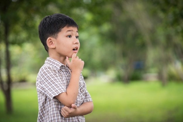 Retrato de la pequeña mano asiática linda del muchacho debajo de la barbilla y pensamiento mientras que se coloca
