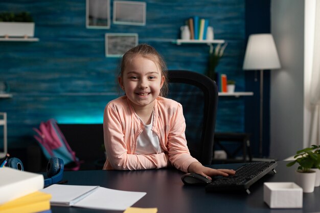 Retrato del pequeño alumno sonriente sentado en la mesa de escritorio en la sala de estar