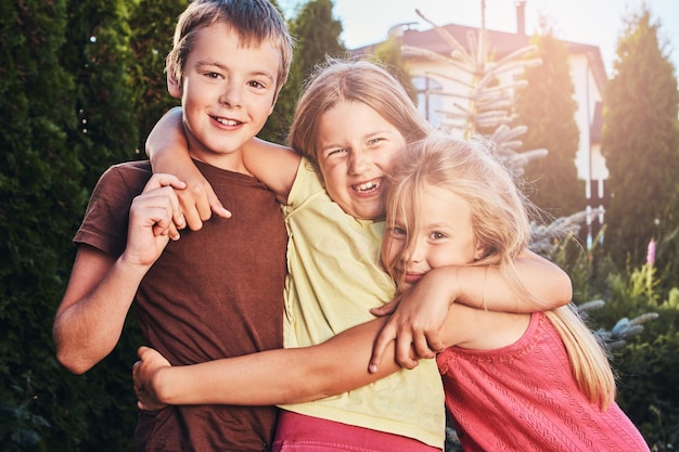 Retrato de pequeños amigos felices divirtiéndose en el patio. Tres lindos amiguitos abrazados y jugando.