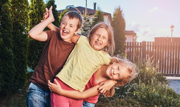 Retrato de pequeños amigos felices divirtiéndose en el patio. Tres lindos amiguitos abrazados y jugando.