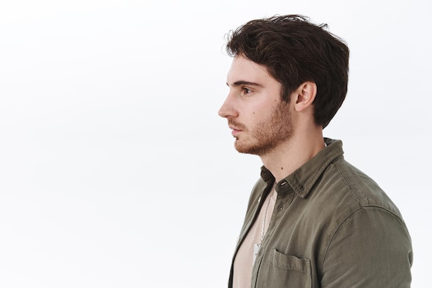 Retrato de perfil de un chico caucásico ordinario con cerdas mirando a la izquierda en el espacio de la capa blanca en blanco sin emociones expresión casual de pie en la cola esperando a alguien y el concepto de promoción