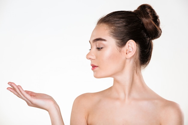 Retrato de perfil de hermosa mujer joven con piel fresca posando mostrando producto en su espacio de copia de palma