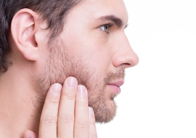 Retrato de perfil de hombre joven guapo con la mano cerca de la cara en la pared blanca.