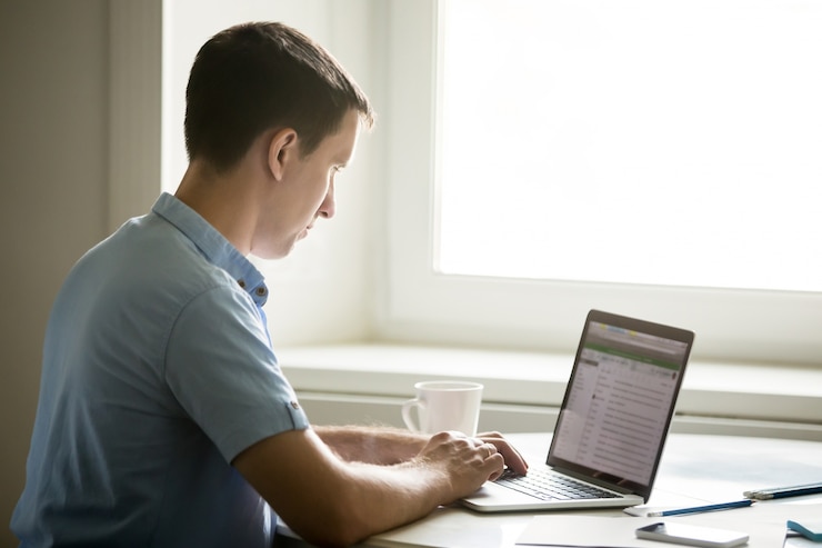Foto gratuito retrato de perfil de un joven trabajando en un escritorio con una computadora portátil
