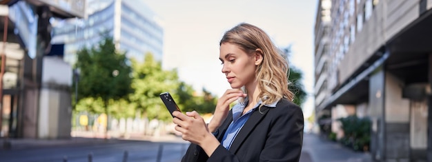 Foto gratuita retrato de perfil de una joven vendedora corporativa en traje usando un teléfono móvil leyendo en un teléfono inteligente