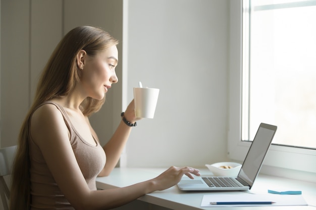 Retrato del perfil de una mujer con la computadora portátil en travesaño de la ventana