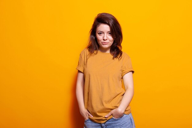 Retrato de persona alegre posando con confianza, tomados de la mano en los bolsillos de los pantalones vaqueros. Mujer caucásica sentirse positivo y de pie sobre fondo naranja, mirando a la cámara. Adulto seguro