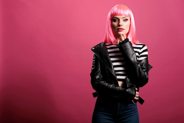 Retrato de una persona feliz con chaqueta de cuero y peinado divertido posando frente a la cámara. Atractiva mujer sensual con estilo de moda, sintiéndose despreocupada y segura en el estudio.