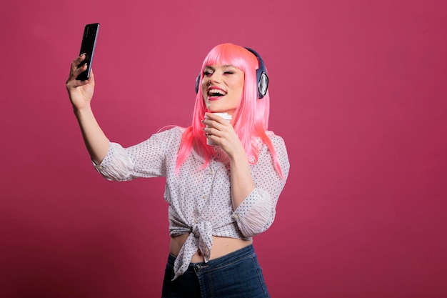 Retrato de una persona genial escuchando música y tomando fotos, usando una aplicación de teléfono móvil para divertirse con las fotos. Haciendo fotografía y auriculares inalámbricos, sintiéndome feliz y positivo.