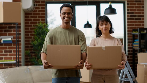 Retrato de personas casadas que se mudan a un departamento alquilado, comenzando nuevos comienzos para el futuro. Sentirse positivo acerca de la reubicación en el hogar, llevando paquetes de contenedores de cartón.