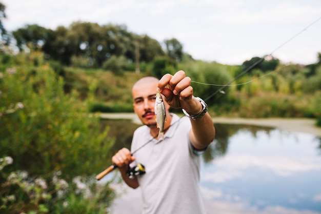 Retrato de un pescador sosteniendo pescado fresco contra el lago