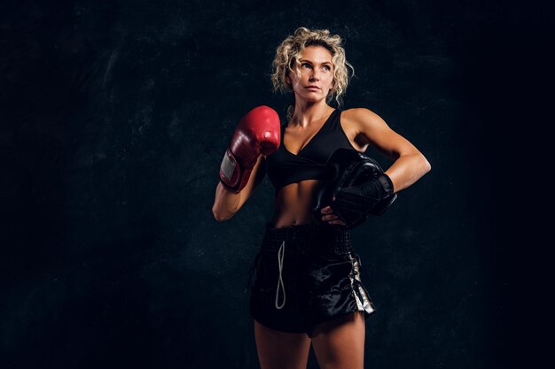 Retrato de una poderosa boxeadora fuerte con guantes rojos sobre fondo oscuro.