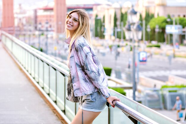 Retrato de primavera soleado positivo brillante de mujer rubia feliz posando en la plaza de Barcelona, vistiendo ropa deportiva de moda hipster