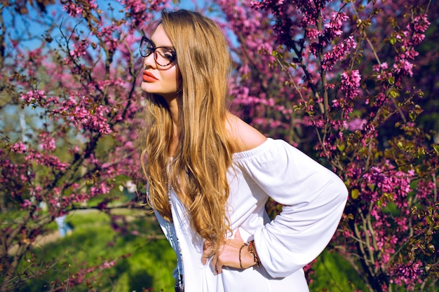 Retrato de primavera verano de mujer joven impresionante con pelos largos naturales asombrosos y rostro de belleza de cerca, con gafas transparentes, colores soleados.