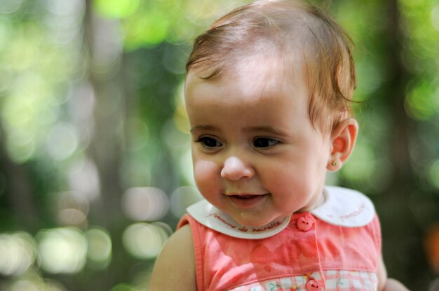 Retrato del primer de la niña de seis meses que sonríe al aire libre con el fondo defocused.