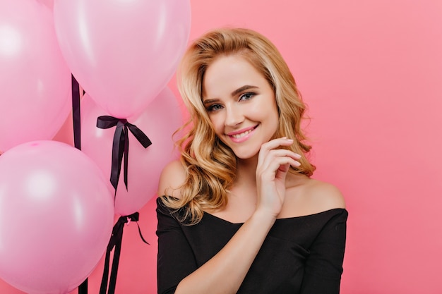 Retrato de primer plano de la adorable cumpleañera rubia. alegre dama rubia en negro posando con globos de fiesta.