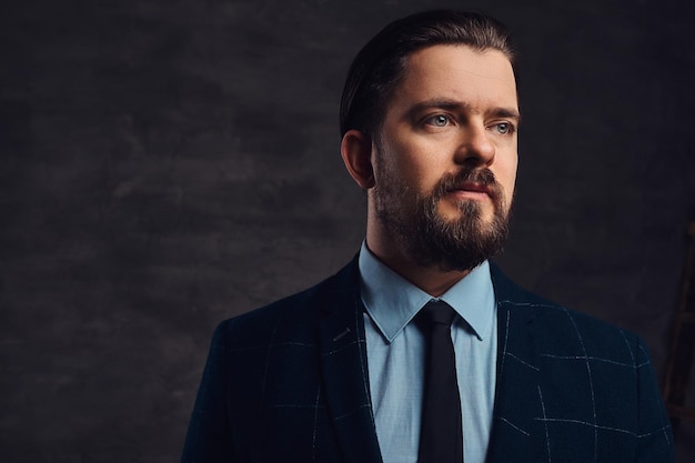 Retrato de primer plano de un apuesto hombre de mediana edad con barba y peinado vestido con un elegante traje formal sobre un fondo oscuro texturizado en el estudio.