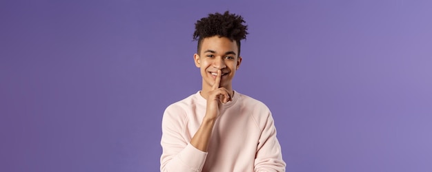 Retrato de primer plano de un atractivo joven sonriente que esconde un secreto que pide guardar silencio o silencio para hacer sur