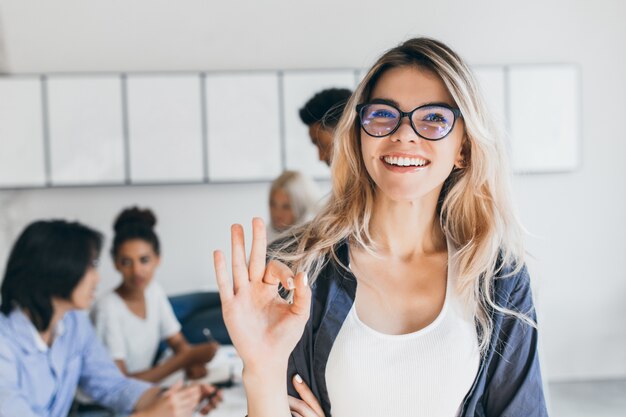 Retrato de primer plano de bastante mujer gerente del departamento de ventas. Foto interior de mujer sonriente que trabaja en la oficina con discutir personas.