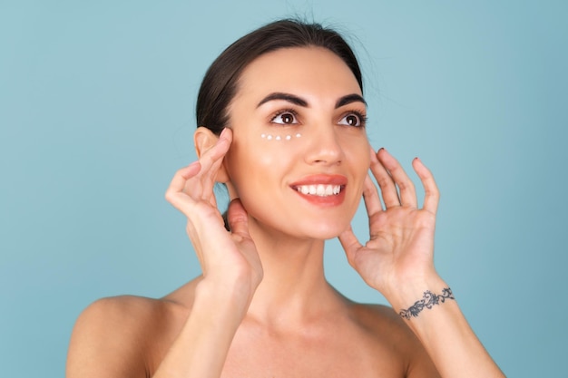 Retrato de primer plano de la belleza de una mujer en topless con piel perfecta y maquillaje natural, con puntos de crema anti-envejecimiento para hidratar y reafirmar la piel debajo de los ojos