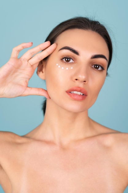 Foto gratuita retrato de primer plano de la belleza de una mujer en topless con piel perfecta y maquillaje natural, con puntos de crema anti-envejecimiento para hidratar y reafirmar la piel debajo de los ojos